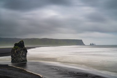 Arkasında Reynisdrangar deniz yığınları olan Dyrholaey 'deki İzlanda kıyılarının siyah kumlu sahili.