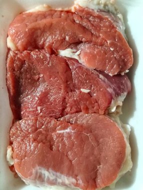 Beyaz köpük tepside düzgünce dizilmiş üç taze kırmızı et bifteğinin dikey yakın plan görüntüleri..