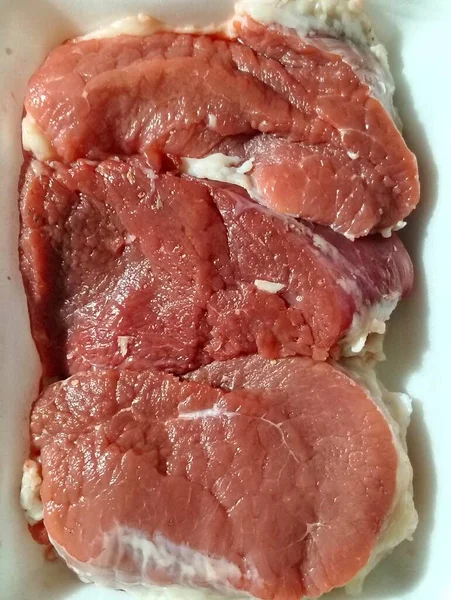 Beyaz köpük tepside düzgünce dizilmiş üç taze kırmızı et bifteğinin dikey yakın plan görüntüleri..