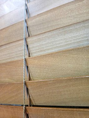 Close-up of wooden window blinds with slats partially open, allowing light to filter through
