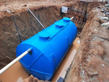 Çamurlu bir hendeğe yerleştirilmiş mavi foseptik tankı.