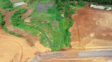 Ağaçları ve bitkileri olan yeşil bir bölgenin yanındaki inşaat alanının havadan görüntüsü.