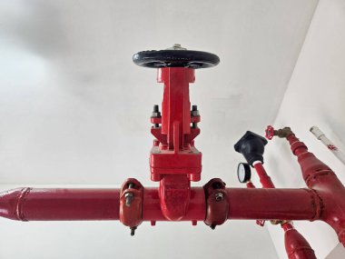 Kırmızı yangın söndürme sistemi vanası ve beyaz duvara dayanan borular..