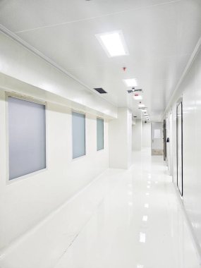Uzun, steril, beyaz bir koridor aydınlatma ve sağ tarafında kapılar var..