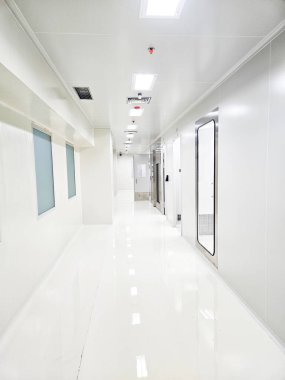 Solunda pencereler, sağında kapılar olan uzun, temiz ve parlak beyaz bir koridor..