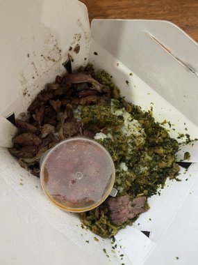 Dilimlenmiş sığır eti, pirinç ve küçük bir sosla servis edilen yeşil sebze karışımıyla dolu bir paket servis kutusu..