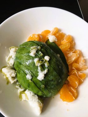 Yarım avokado, parçalanmış beyaz peynir ve parlak turuncu mandalina segmentleriyle dolu beyaz bir kâsenin yakın plan çekimi taze ve canlı bir yemek oluşturur..