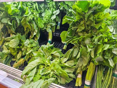 Taze yeşil yapraklı sebzeler, muhtemelen ıspanak ya da amaranth, güzelce paketlenmiş ve bir markette sergileniyor..