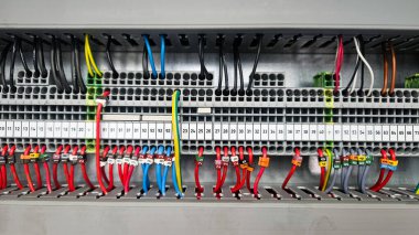 Terminal bloklarına bağlı çeşitli renkli kablolarla organize bir elektrik kontrol panelinin yakın görüntüsü.