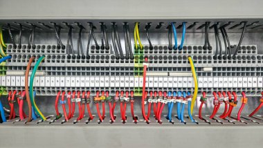 Terminal bloklara bağlı çok renkli kablolarla endüstriyel elektrik kontrol panelinin yakın görüntüsü, karmaşık kabloları ve organizasyonu gösteriyor.