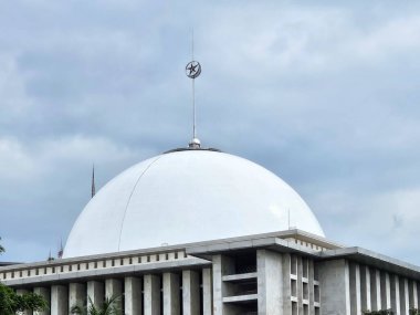Büyük beyaz kubbenin yakın görüntüsü ve bulutlu bir gökyüzünün altındaki modern bir caminin kulesi..