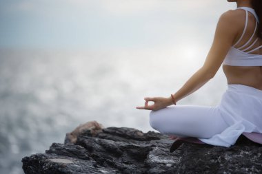Sukhasana egzersizinde yoga yapan Asyalı genç bir kadın denize bakarken....