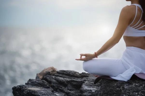 Sukhasana egzersizinde yoga yapan Asyalı genç bir kadın denize bakarken....