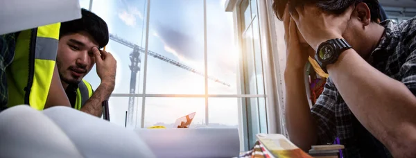 Stressful of engineer people in panic while meeting at the office, Young employee holding hands on his head with stress while sitting at the desk. Construction Business Banner background.