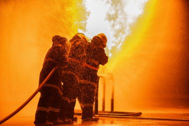 Yangın söndürücü ya da hortumdan su püskürtmek için yangın söndürücü kullanan itfaiyeci. Yangın alevleriyle savaşmak ve sanayi bölgesinde güvenliği sağlamak için yangın söndürücü kullanıyor..