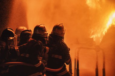 Yangın söndürücü ya da hortumdan su püskürtmek için yangın söndürücü kullanan itfaiyeci. Yangın alevleriyle savaşmak ve sanayi bölgesinde güvenliği sağlamak için yangın söndürücü kullanıyor..