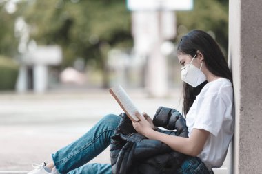 Koronavirüs salgını sırasında açık havada bulaşıcı hastalıklara karşı maske takan liseli öğrenciler okulda yalnız başlarına okuyorlar. Öğrencilerin yeni normal hayatı.