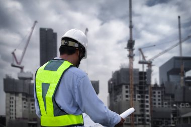İnşaat alanındaki Mühendislik Danışmanlığı elinde planları tutuyor. İnşaat müfettişi. Yeni binanın inşaat sahası çizimi ve iş akışı