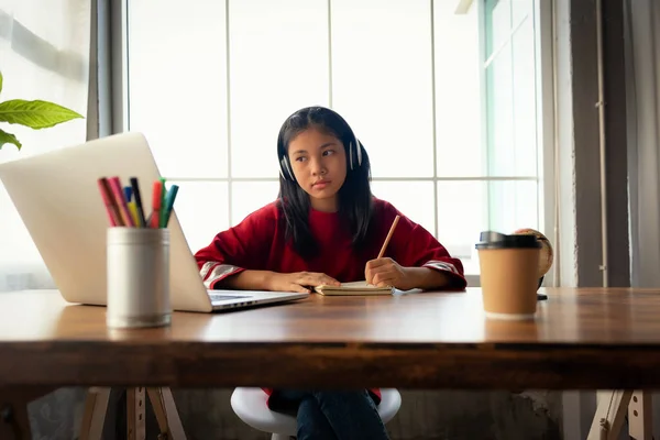 Female student wears headphones and looking to laptop computer study online listen to watch teacher at home for Studying through online E-learning system in training course. Distance education concept.