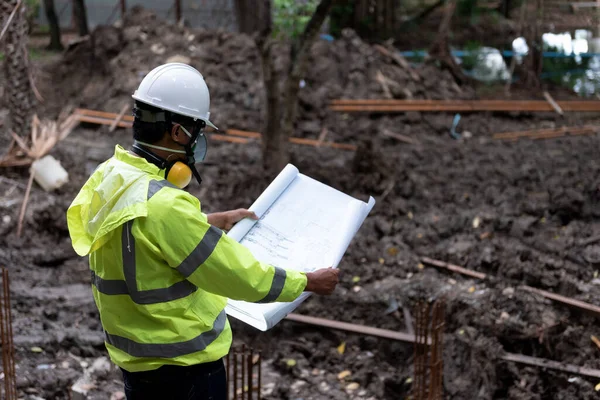 Civil Engineer People wearing safety helmet while inspection detail on construction site with drawing blueprint. Surveyor and checking building foundation structure on soil.