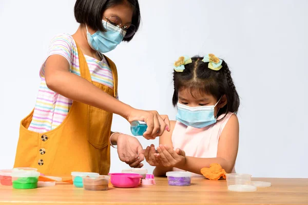 Asian children wear face mask while cleaning hands with alcohol gel, Hand cleaning every playing together in new normal life of children. Coronavirus protective for kids.