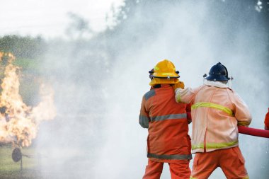 İtfaiyeci yangın söndürme hortumundan su püskürtmek için bir yangın söndürücü kullanıyor. Yakıt için alevle savaşıyor ve güvenlik için yangını kontrol ediyor. Sanayide itfaiyeciyi eğitmek.