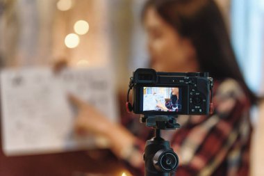 Tripoddaki dijital kameranın fotoğrafını kapat ve Asyalı bir kadın video kamerada blog için kayıt öğretiyor. Evde çalışır, dijital kamera üzerine odaklanır İletişim ve eğitim kavramı.