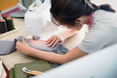 Kurgu stüdyosunda dikiş makinesiyle çalışan Asyalı genç kadın terzi. Dikiş makinesiyle kumaş malzemesini beslerken ellerinin üzerinde çok sığ bir odak noktası var..
