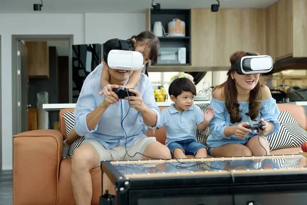 Asian family sitting playing games using virtual reality VR headset together in the living room at home, a cheerful family enjoying active funny together. Family time concept