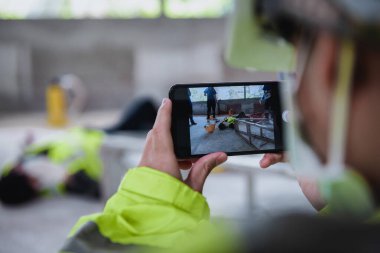 İnşaat alanındaki işyerinde çalışan işçilerin bilinci yerinde değilken, tıbbi yardım ekipleri ekipmanlarıyla kazalara akıllı telefon ateşi açtılar..