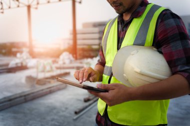 İnşaat alanındaki Mühendislik Danışmanı elinde tablet tutuyor. İnşaat Projesinde BIM teknolojisine sahip iş akışı ve inşaat müfettişi yönetimi.