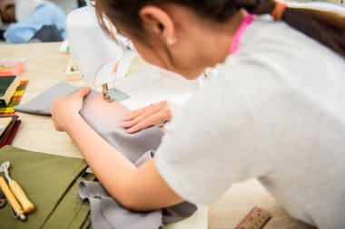 Kurgu stüdyosunda dikiş makinesiyle çalışan Asyalı genç kadın terzi. Dikiş makinesiyle kumaş malzemesini beslerken ellerinin üzerinde çok sığ bir odak noktası var..