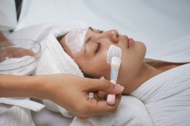 Asyalı genç kadınlar maske fırçası kullanarak rahatlar, ciltlerini nemlendirir, ciltlerini nemlendirir, ciltlerini nemlendirir, yüz maskesi takmalarına yardımcı olur. Evde boş zaman aktivitesi.