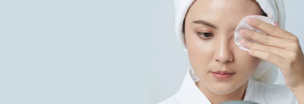 Asian young woman using cosmetic pad or cotton pad remove makeup cares for face skin., Banner size with copy space.