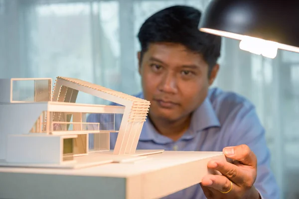 Architect-designer holding model of modern box house while thinking about concept of building and construction project before startup in the future. Focusing on modern box house model.