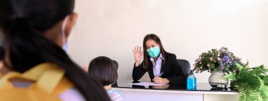 Öğretmen Coronavirus önleme için sınıfa girmeden önce anaokulu öğrencilerinin verilerini tarıyor ve kaydediyor. Evden okula geçişin bir parçası olarak yeni sosyal etkileşim.