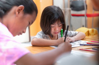 Asyalı küçük kız oturma becerilerini geliştirip masadaki boyama kağıdına odaklanıyor. Anaokulu öğrencileri evde yazmayı ve okumayı, sanat eğitimini ve yaratıcılığı, çocukların faaliyetlerini öğrenirler..