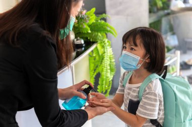 Öğretmen el dezenfektanına alkol jeli veriyor ve okulda sağlıklı ve temiz kalmak için öğrencilere yardım ediyor. Sınıfa girmeden önce öğrenci gösterimi.