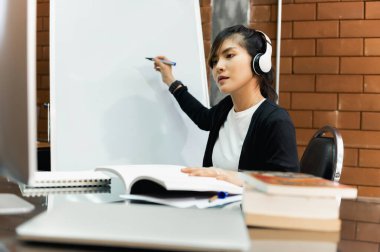 Asyalı öğretmen online masada oturuyor ya da sınıftaki öğrencilere beyaz tahtayla ders veriyor. Modern eğitim, karantina eğitimi, Çevrimiçi eğitim kavramı.