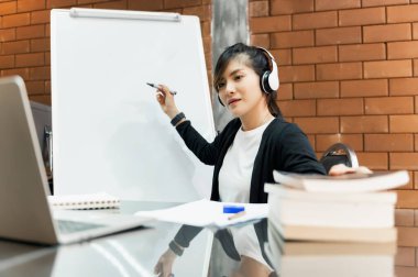 Asyalı öğretmen online masada oturuyor ya da sınıftaki öğrencilere beyaz tahtayla ders veriyor. Modern eğitim, karantina eğitimi, Çevrimiçi eğitim kavramı.