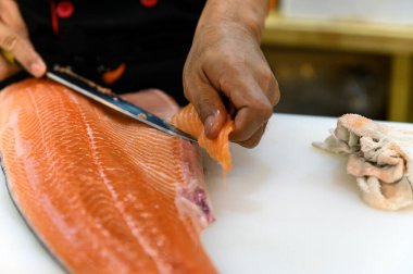 Taze somon filetosu, yemek odasında somon balığını karnından fileto yaparken beyaz kesim masasının üzerinde duruyor. Yumuşak odaklı somon filetosuna odaklanan seçim.
