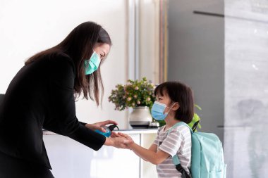 Öğretmen el dezenfektanına alkol jeli veriyor ve okulda sağlıklı ve temiz kalmak için öğrencilere yardım ediyor. Sınıfa girmeden önce öğrenci gösterimi.