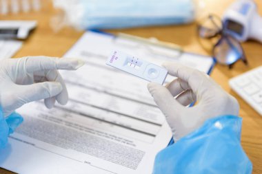 Coronavirus, COVID-19 için hızlı antijen test kiti taşıyan doktor veya hemşirelerin elleri, hastane, revir, Hastalık ve Kamu Sağlığı Hizmetleri konseptinde masa başı muayenesi sırasında.