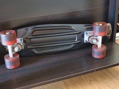 Siyah bir mini kaykay siyah bir ahşap rafta duruyor. İç mekan yaşam tarzı ve boş zaman aktivitesi.