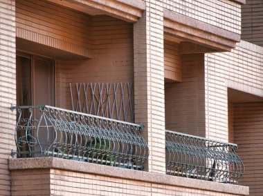 Süslü demir parmaklıklı iki şehir balkonu, kahverengi tuğlalı bir binanın ön cephesine kurulmuş. Şehir mimarisi, ikamet yeri, dış tasarım.