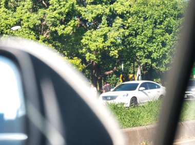 Yolun kenarına park edilmiş beyaz bir araba, bir arabanın camından görülüyor. Şehir ortamı, günlük yaşam, şehir manzarası..