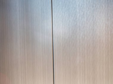 Modern endüstriyel estetiği gösteren iki desenli paneli birbirinden ayıran belirgin dikey bir çizgiyle gümüş fırçalı metalik bir yüzeye yakından bakmak..