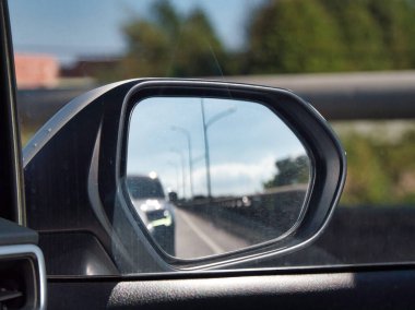 Bir yan aynanın içinden bir otoyolu yansıtan ve parlak bir gökyüzünün altında geçen araçların hareketini ve seyahat perspektifini yakalayan bir arabanın görüntüsü.