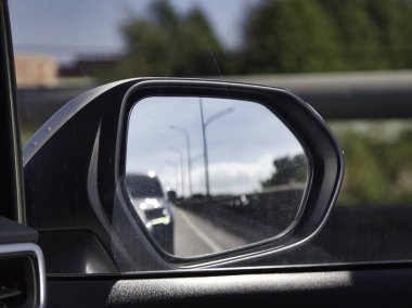 Bir yan aynanın içinden bir otoyolu yansıtan ve parlak bir gökyüzünün altında geçen araçların hareketini ve seyahat perspektifini yakalayan bir arabanın görüntüsü.