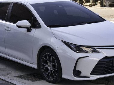 Şehir merkezinde asfalt bir sokağa park edilmiş modern bir beyaz sedan, gösterişli tasarım ayrıntıları ve koyu renkli pencerelerle, çağdaş bir tarz ve günlük işe gidiş-dönüş hissini aktarıyor..